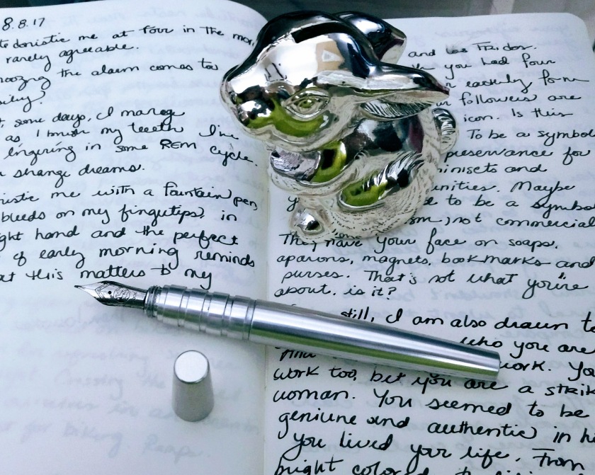 silver fountain pen resting on a journal with cursive handwriting